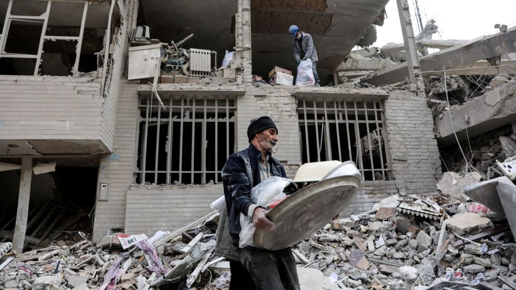 Image of a man walking amid rubble after a military strike in Iran