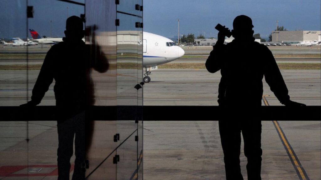 A passenger holds a mobile phone while looking at a commercial airplane at San Francisco International Airport in San Francisco, California, U.S., November 6, 2025. (Reuters/Carlos Barria)