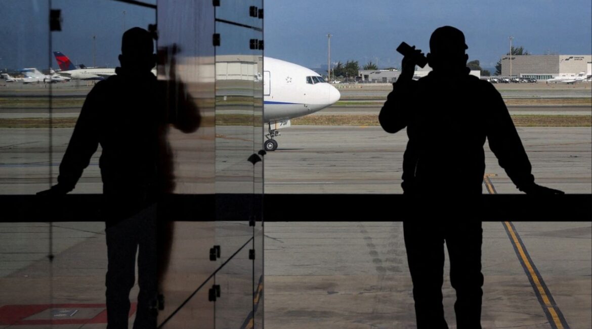 A passenger holds a mobile phone while looking at a commercial airplane at San Francisco International Airport in San Francisco, California, U.S., November 6, 2025. (Reuters/Carlos Barria)