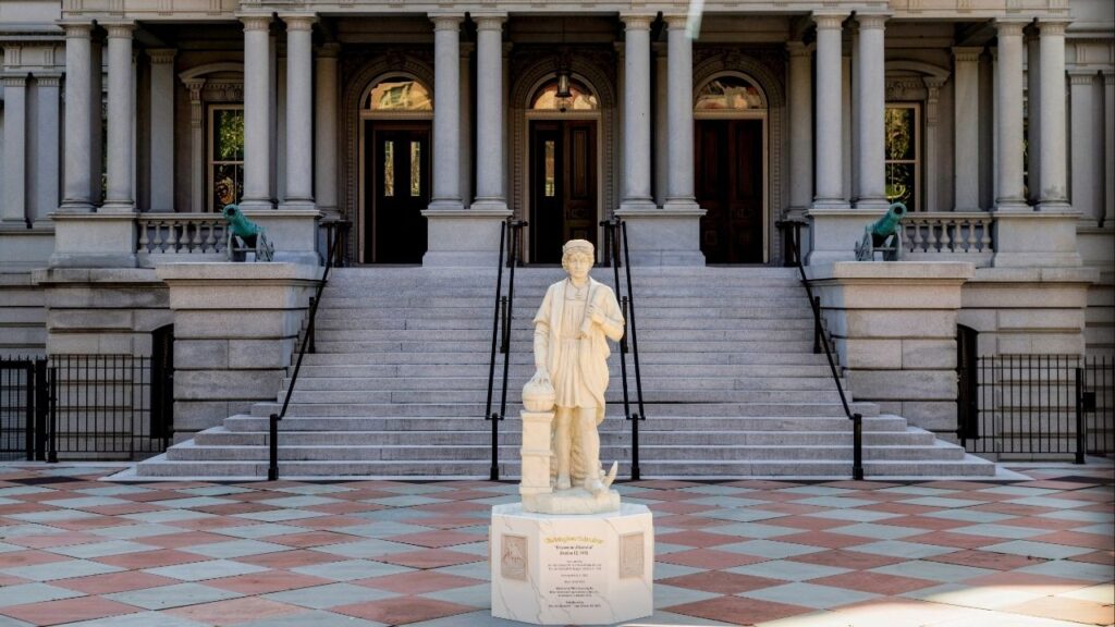 A statue of Christopher Columbus stands in front of the Eisenhower Executive Office Building at the White House Complex in Washington after being installed early Sunday morning, March 22, 2026. A statue of Christopher Columbus was installed on the grounds of the White House early Sunday morning, as part of President Trump’s effort to position the explorer as a hero after monuments to him were removed across the country. (Jason Andrew/The New York Times)