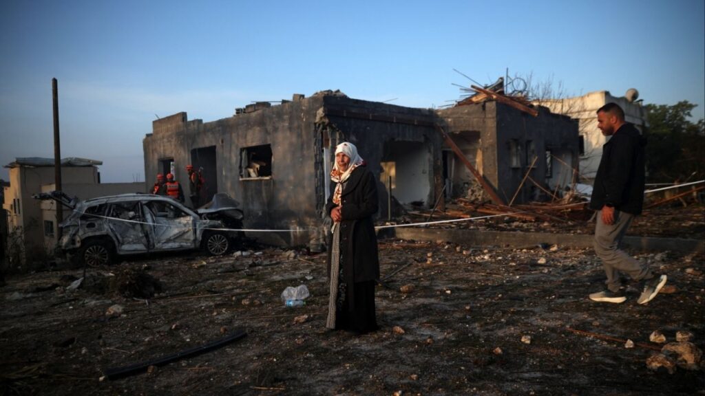 A woman stands as Israeli emergency responders work at the site of an impact by an Iranian missile, amid the U.S.-Israel conflict with Iran, in northern Israel, March 13, 2026. (Reuters/Shir Torem)