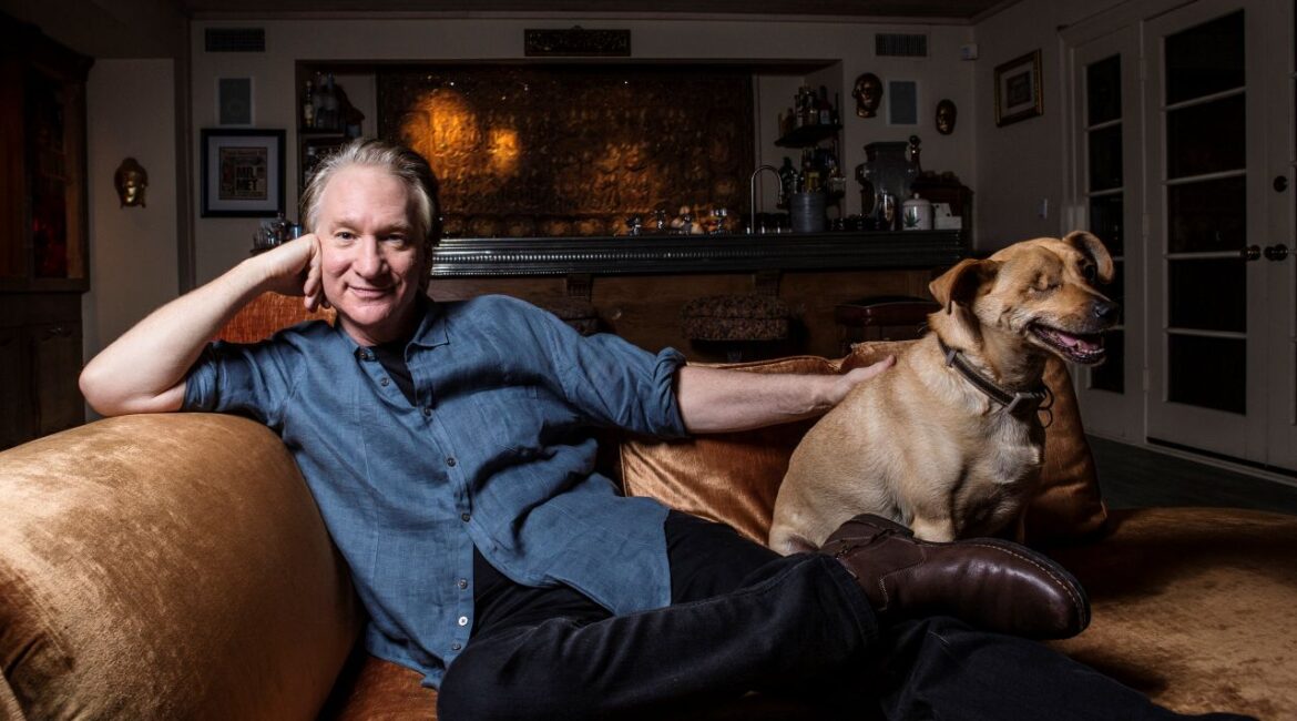 Image of Bill Maher at home with his dog. They're both sitting on a sofa.