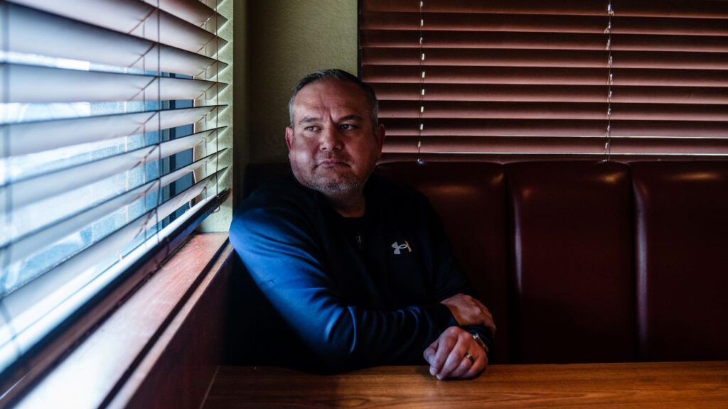 Portrait image of conservative Wasco City Councilmember Vince Martinez, dressed in blue, sitting at a table and looking out the window