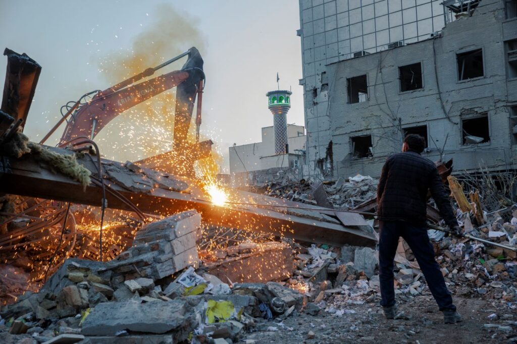 Image of workers and equipment used to break up a debris pile in Tehran, Iran, after a US-_Israeli missile strike