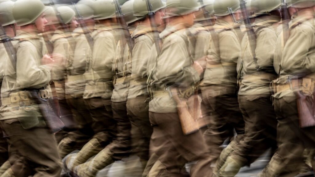 Blurred image of U.S Army soldiers wearing helmets and carrying rifles marching in a parade