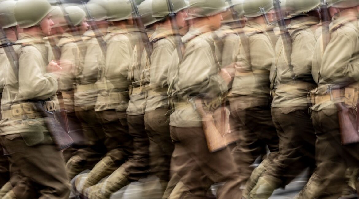 Blurred image of U.S Army soldiers wearing helmets and carrying rifles marching in a parade