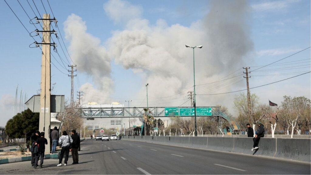 People gather on the sides of a road as smoke rises in the background following an explosion, amid the U.S.-Israeli conflict with Iran, in Tehran, Iran, March 5, 2026. (Majid Asgaripour/WANA (West Asia News Agency) via Reuters)