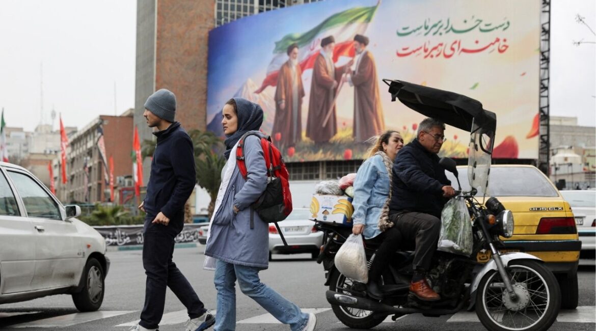 People walk on a street with a banner of Iran's new supreme leader Mojtaba Khamenei with late supreme leader Ayatollah Ali Khamenei and late supreme leader Ayatollah Ruhollah Khomeini in the background, amid the U.S.-Israeli conflict with Iran, in Tehran, Iran, March 10, 2026. (Majid Asgaripour/WANA (West Asia News Agency) via Reuters)