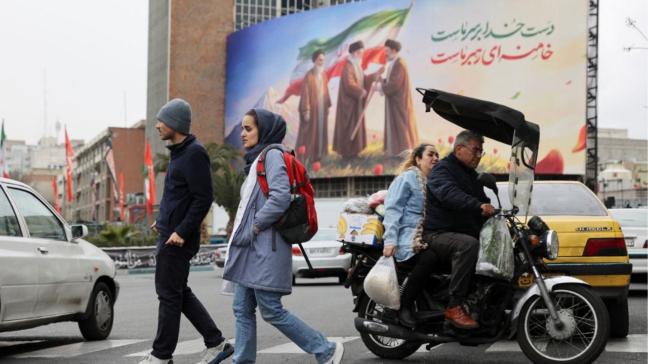People walk on a street with a banner of Iran's new supreme leader Mojtaba Khamenei with late supreme leader Ayatollah Ali Khamenei and late supreme leader Ayatollah Ruhollah Khomeini in the background, amid the U.S.-Israeli conflict with Iran, in Tehran, Iran, March 10, 2026. (Majid Asgaripour/WANA (West Asia News Agency) via Reuters)
