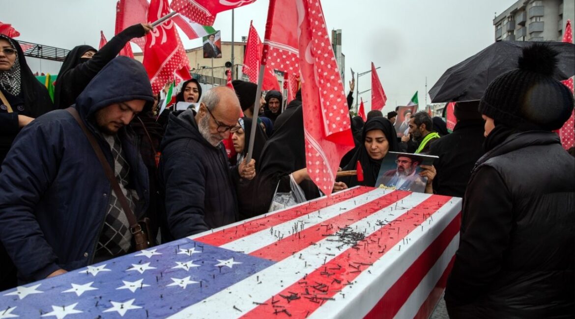 Supporters of the Iranian government hammer nails into a coffin draped with a United States flag during a rally in Tehran marking Quds Day, an event held annually by the Iranian government to oppose Israel, on the last Friday of Ramadan, March 13, 2026. An explosion was seen on Friday close to where crowds had gathered in Tehran for a rally, according to videos shared by Iranian state television. It was not immediately clear what had caused the explosion. (Arash Khamooshi/The New York Times)
