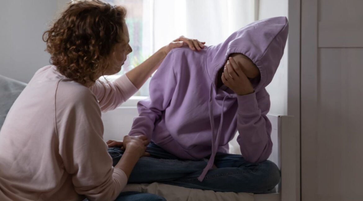 Image of a woman comforting a teen who has his handover his face