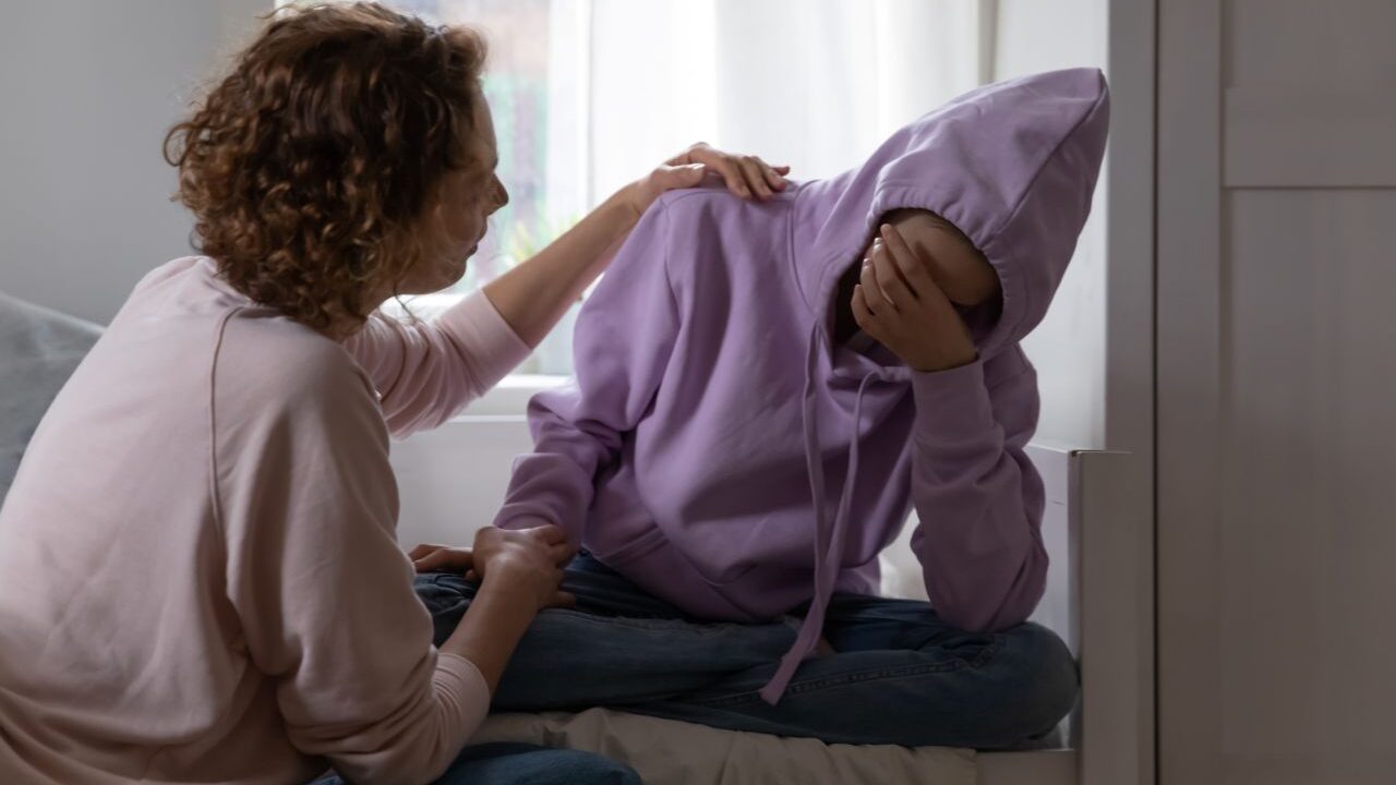 Image of a woman comforting a teen who has his handover his face