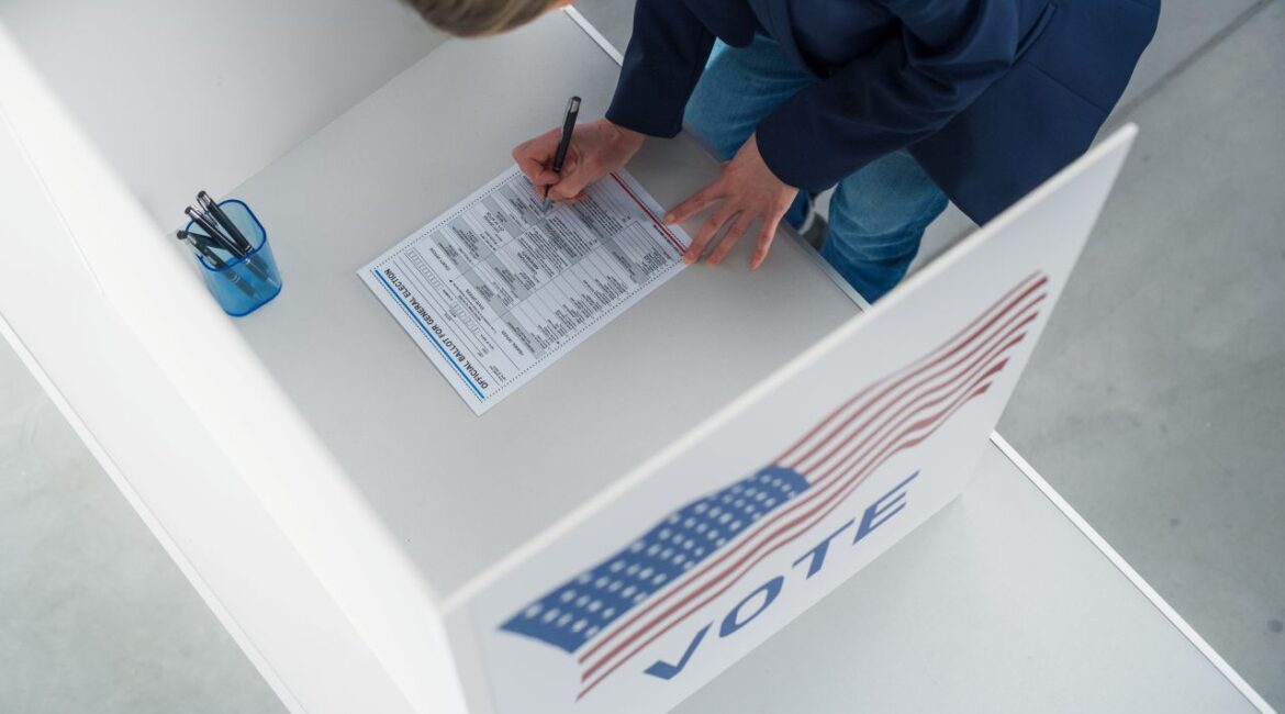 Image of a person filling out an election ballot in a booth with an American flag on the side