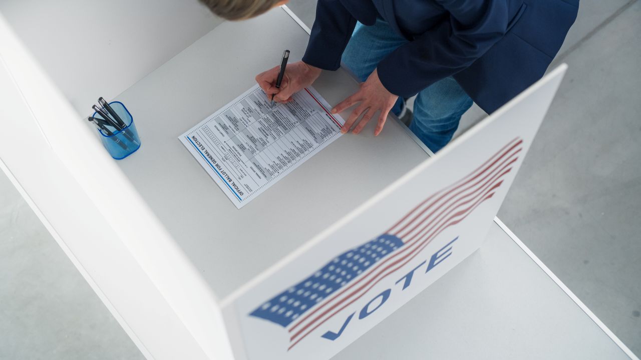 Image of a person filling out an election ballot in a booth with an American flag on the side
