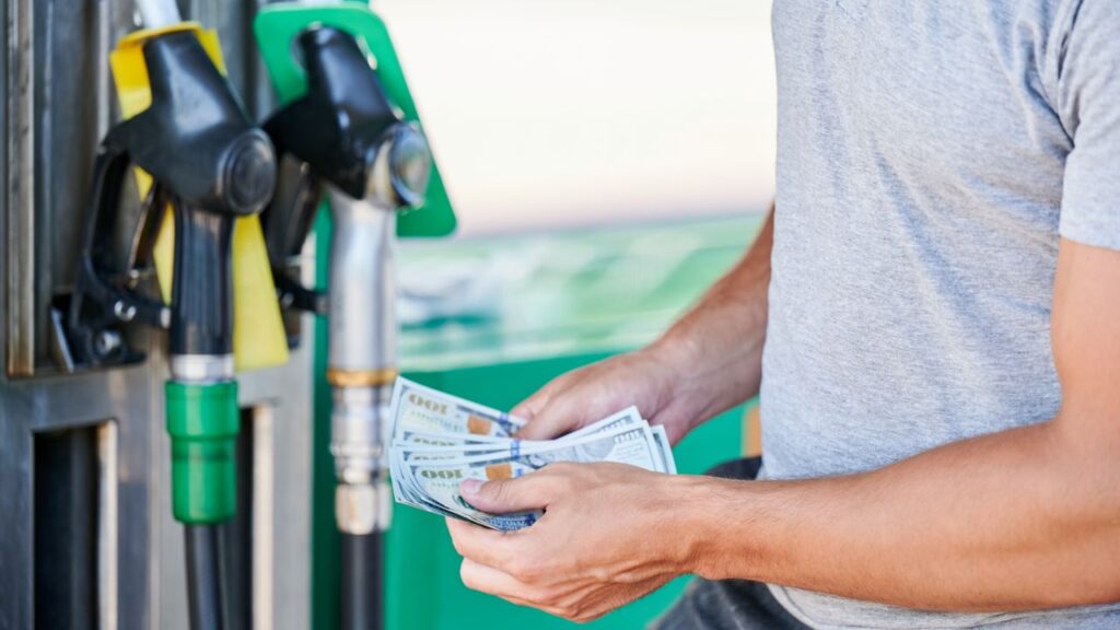 Image of a man holding $100 bills getting ready to buy gasoline at the pup