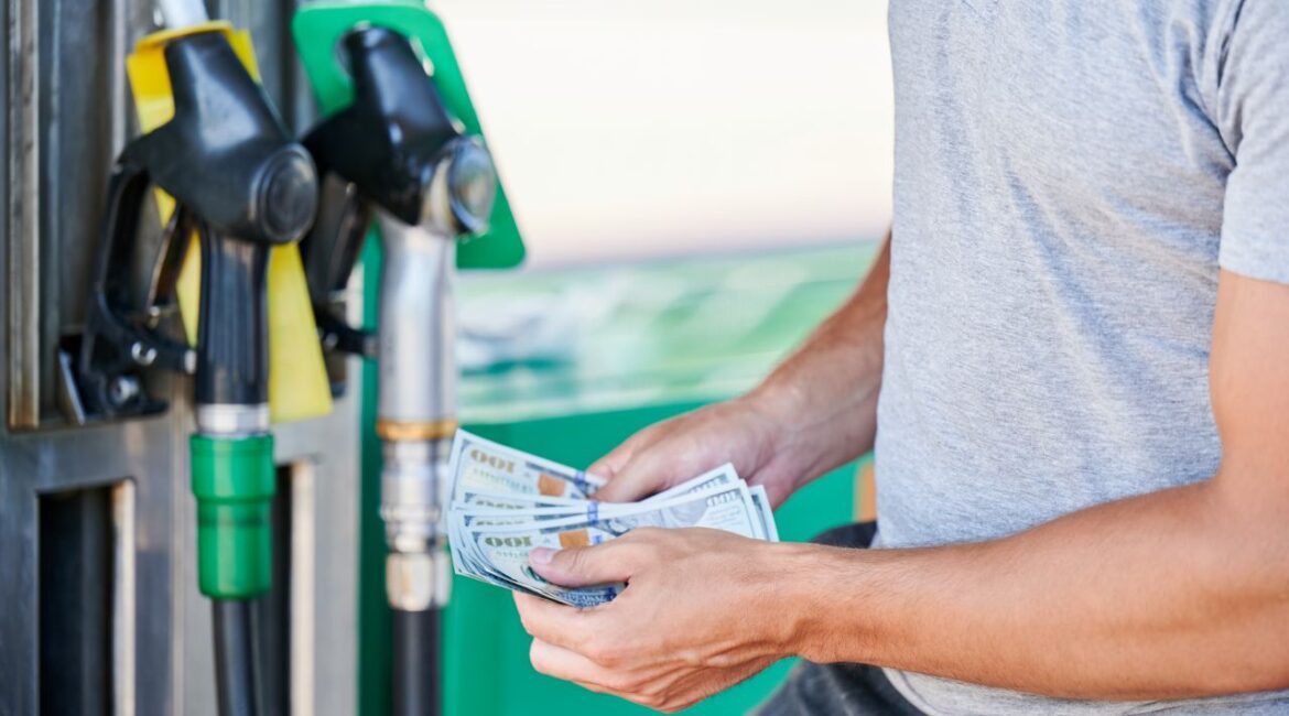 Image of a man holding $100 bills getting ready to buy gasoline at the pup