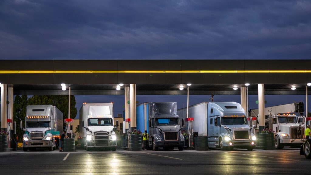 Image of transport trucks lined up at night at a fueling station