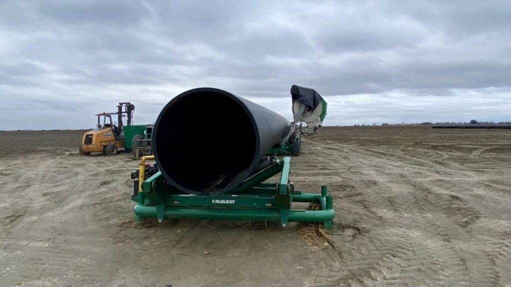 Image of a massive pipe on a piece of heavy equipment on unplanted farmland