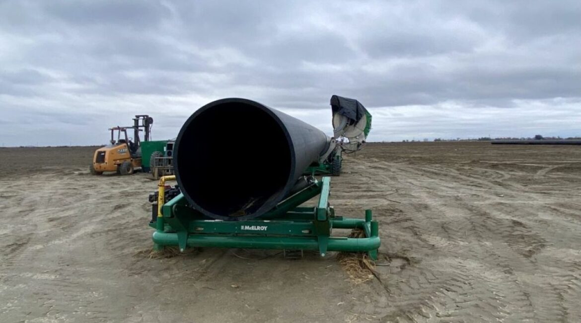 Image of a massive pipe on a piece of heavy equipment on unplanted farmland