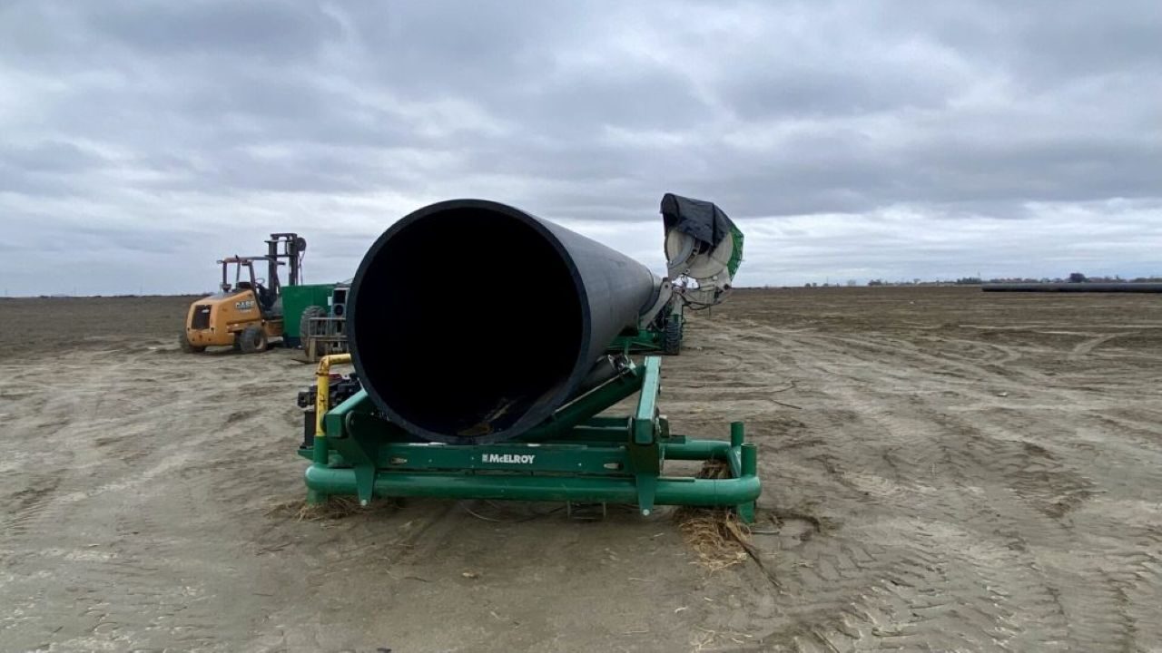 Image of a massive pipe on a piece of heavy equipment on unplanted farmland