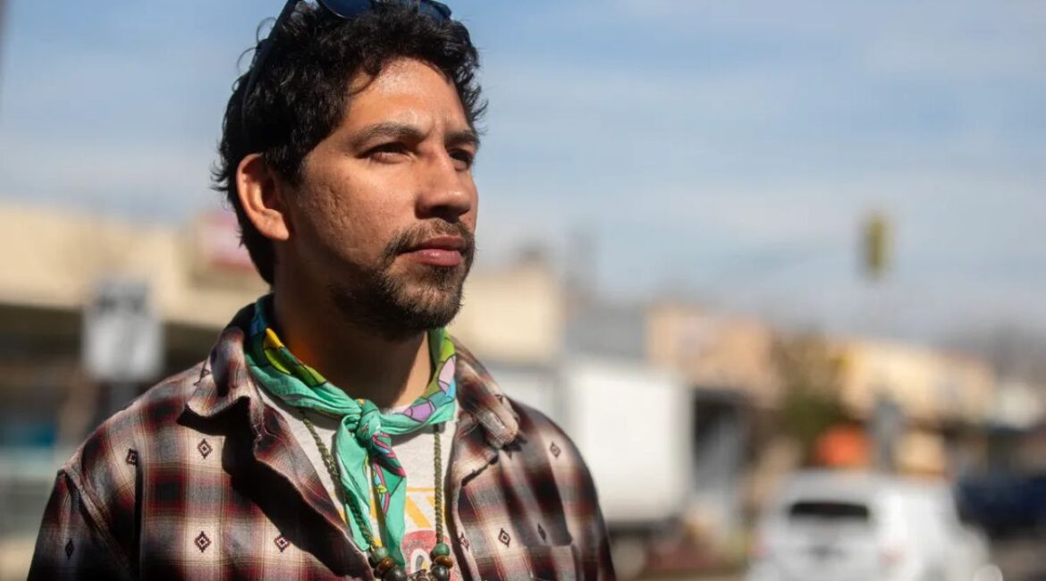 Image of Alfred Aldrete. He's wearing a wool shirt in a Native American pattern, has a beard, a green bandana and jewelry around his neck