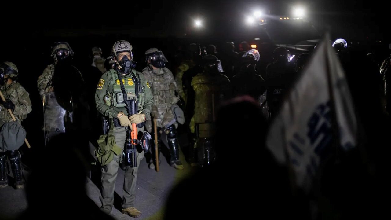 Image of federal immigration agents grouping up at night outside a farm. A few lights provide illumination