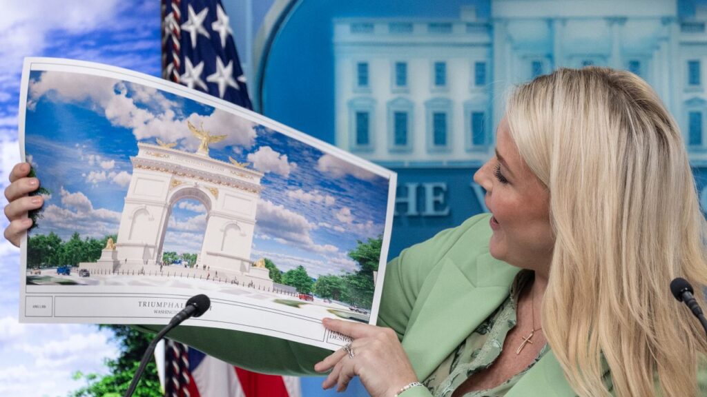 Karoline Leavitt in a pastel green suit looks at the Triumphal Arch rendering during a briefing