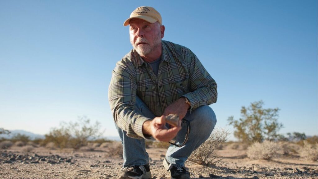 J. Craig Venter studies a rock at the location where his company, Synthetic Genomics, is preparing samples of soil and rock found in the Mojave Desert outside Baker, Calif., Nov. 15, 2013. Venter, a risk-taking outsider who brought speed, competition and controversy to the race to decode the human genome, died in San Diego on Wednesday, April 29, 2026. He was 79. (Michal Czerwonka/The New York Times)