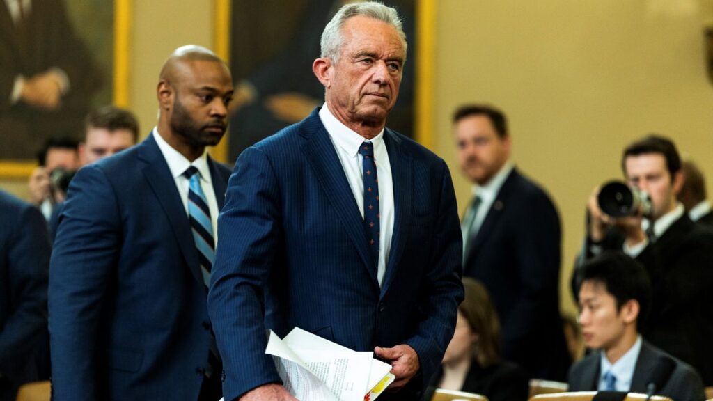 Image of HHS Secretary Rpbert F. Kennedy Jr. before a hearing on Capitol Hill. He's in a blue suit with a white shirt and predominantly blue tie