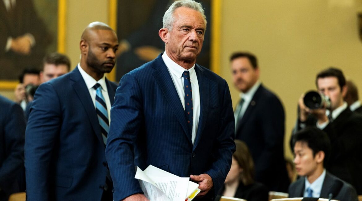 Image of HHS Secretary Rpbert F. Kennedy Jr. before a hearing on Capitol Hill. He's in a blue suit with a white shirt and predominantly blue tie