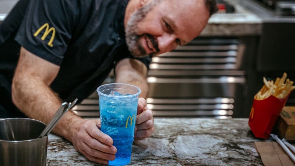 Image of a McDonald's team member demonstrating one of the fast-food giant's new refresher drink. the liquid is bright blue and it's in a clear plastic cup.