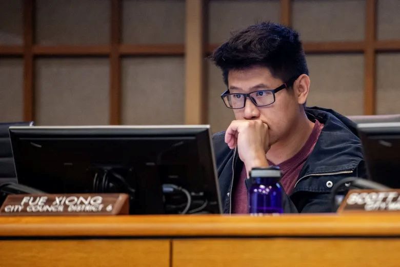 Image of Merced City Councilmember Fue Xiong on the dais, with his hand on his chin and his eyes staring at a computer