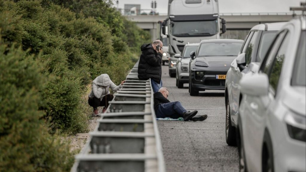 People take cover along a guardrail on a roadway as a siren warns of incoming missiles near Yavne, Israel, March 29, 2026. A majority of Israelis support the war with Iran, but many doubt that it will solve Israel’s long-term security problems. Some also question their prime minister’s assurances and motives. (Avishag Shaar-Yashuv/The New York Times)