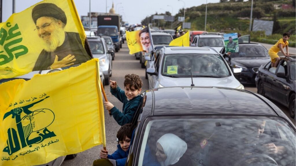 Returnees wave Hezbollah flags bearing pictures of Hasan Nasrallah, the group’s leader killed in the 2024 war, near Ain Abou Abdallah on Friday, April 17, 2026, hours after a cease-fire paused fighting between Israel and Hezbollah. Stuck in standstill traffic, Lebanese people who had been displaced by fighting expressed a mix of excitement and uncertainty about a pause in Israel’s campaign against Hezbollah. (David Guttenfelder/The New York Times)