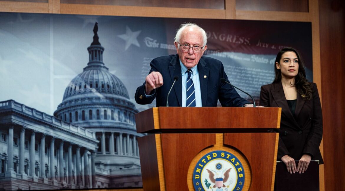 Image Sen. Bernie Sanders speaking at a podium and gesturing with his hand. Rep. Alexandria Ocasio-Cortez is also in the image
