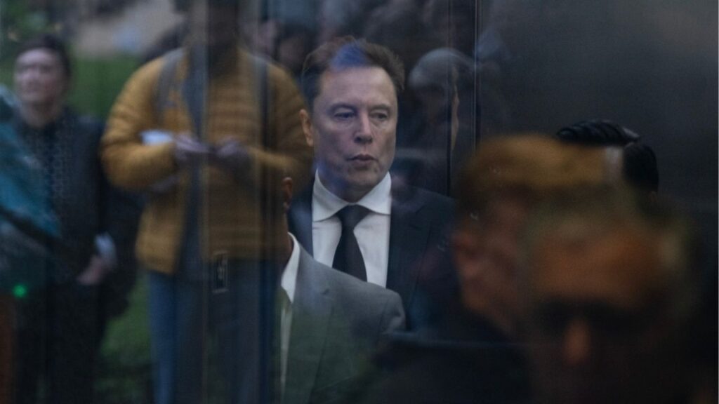 Seen through reflections in glass, Elon Musk arrives at The Ronald V. Dellums Federal Courthouse in Oakland, Calif., the venue for his lawsuit against OpenAI, on Tuesday, April 28, 2026. Musk on Wednesday will again take the stand in his blockbuster case against OpenAI for a second day of testimony in which he has argued the AI company and its founders violated promises it made to him and the public. (Brennan Smart/The New York Times)