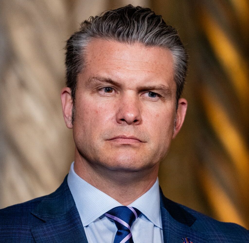 Image of Pete Hegseth in blue suit, blue shirt, with blue and silver striped tie