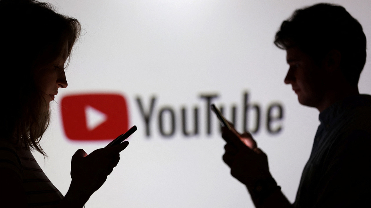 Teenagers pose for a photo while holding smartphones in front of a YouTube logo in this illustration taken September 11, 2025. (Reuters/Dado Ruvic/Illustration)