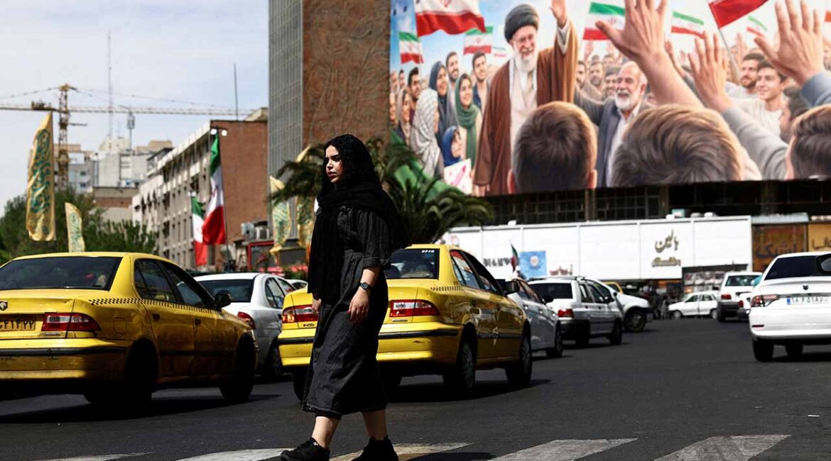 A woman walks past a billboard featuring an image of the late Supreme Leader of Iran, Ayatollah Ali Khamenei, on a building, amid a ceasefire between U.S. and Iran, in Tehran, Iran, April 27, 2026. (Reuters/File Photo)