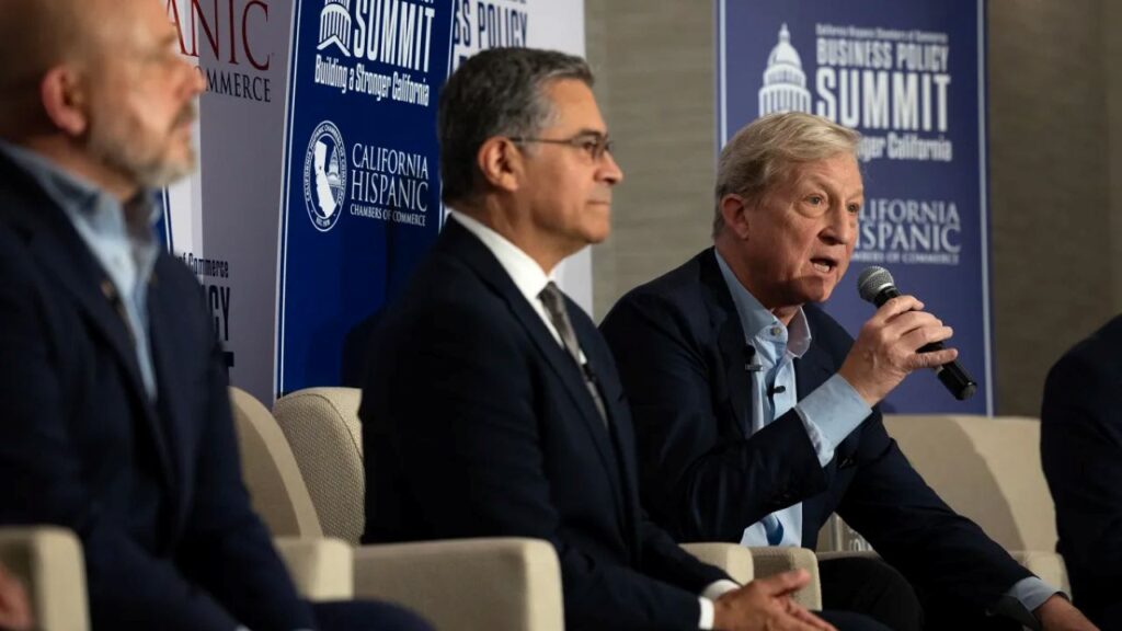 Image of three California governor candidates sitting in yellow chairs on a stage. Candidate Tom Steyer is speaking into a microphone