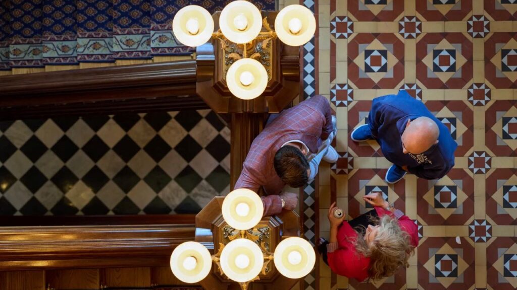 Overhead view of a California lawmaker in a red blazer meeting with lobbyist in the state Capitol