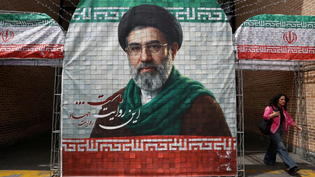 Image of a woman walking past a colorful poster of Iran's new Supreme Leader