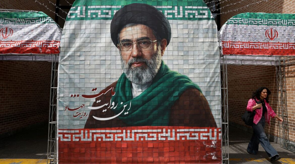 Image of a woman walking past a colorful poster of Iran's new Supreme Leader