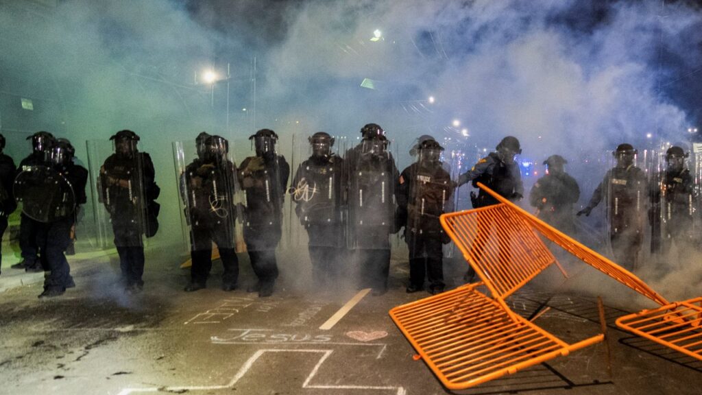 Image if police officers advancing in riot gear amid smoke during a night time action