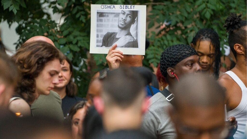 A mourner holds a photo of O’Shae Sible during a memorial and vigil to honor Sibley, a 28-year-old gay man who was fatally stabbed after a dispute over his vogueing in a parking lot, in New York, Aug. 5, 2023. Dmitry Popov was 17 when he stabbed O’Shea Sibley, a 28-year-old dancer, at a gas station on July 29, 2023; he has been charged with murder as a hate crime. (David Dee Delgado/The New York Times)