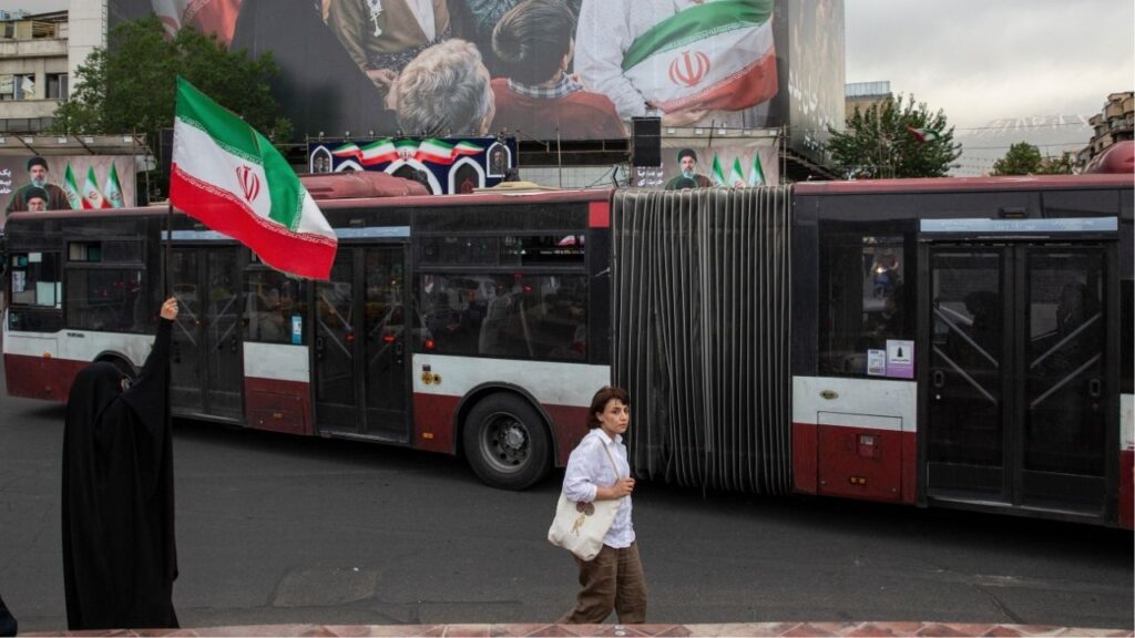 A woman waves an Iranian flag near a new billboard in Enghelab Square in Tehran, May 24, 2026. Iran began restoring internet access for tens of millions of Iranians, a senior official said on Tuesday, lifting a blackout imposed after the U.S. and Israel launched military strikes on the country on Feb. 28. (Arash Khamooshi/Polaris for The New York Times)