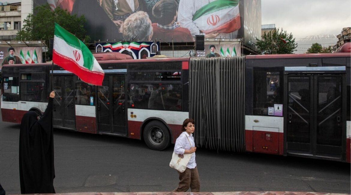 A woman waves an Iranian flag near a new billboard in Enghelab Square in Tehran, May 24, 2026. Iran began restoring internet access for tens of millions of Iranians, a senior official said on Tuesday, lifting a blackout imposed after the U.S. and Israel launched military strikes on the country on Feb. 28. (Arash Khamooshi/Polaris for The New York Times)
