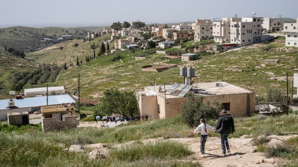 Image of a man and a girl walking in the West Bank on a trail leading houses amid green grass
