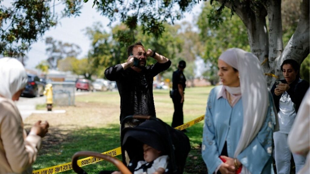 Members of the Muslim community use their phones at the scene of a reported active shooter situation at the Islamic Center, with yellow tape placed behind them to cordon the area, in San Diego, California, U.S., May 18, 2026. REUTERS/Mike Blake