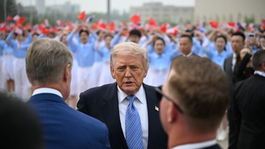Image of Donald Trump during a departure ceremony after his summit in China. He's wearing a dark blue suit, white shirt, and light blue tie and facing the camera